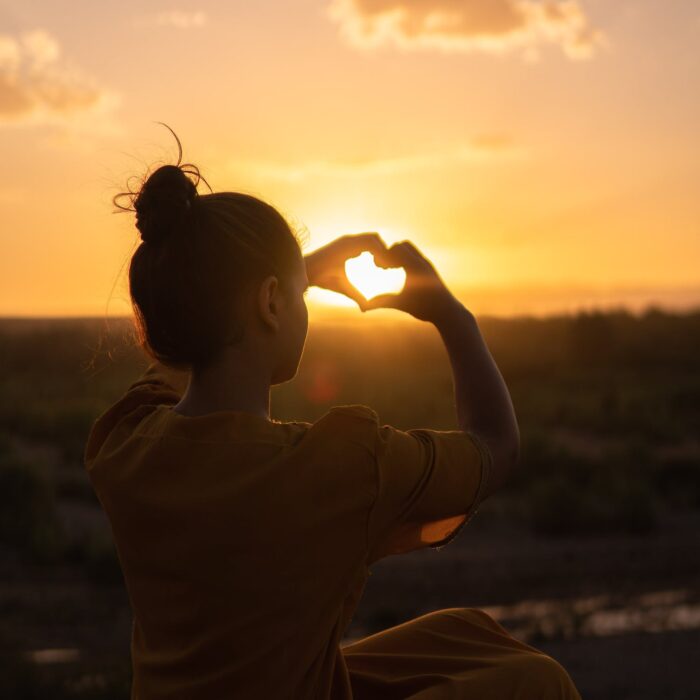 woman creating a heart with her hands in the sun influencer