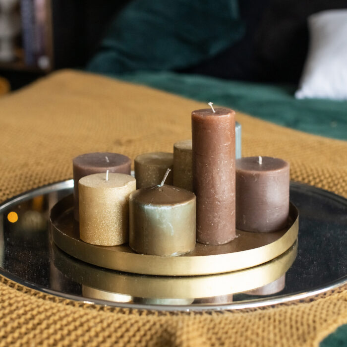 A tray with a set of brown candles stands on a bed with a blanket