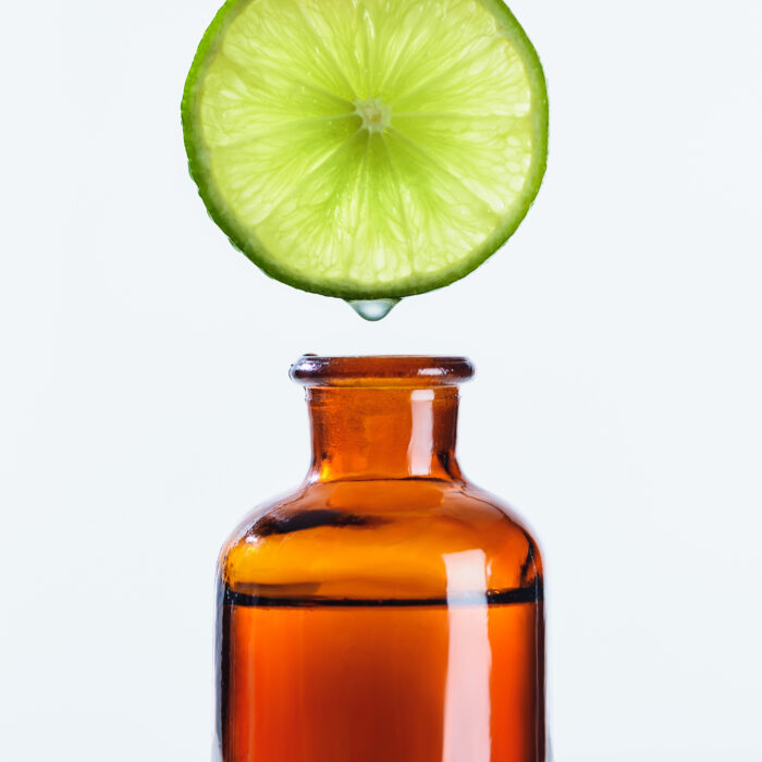 Aromatic juice of lime piece dripping into bottle of natural herbal essential oil isolated on white