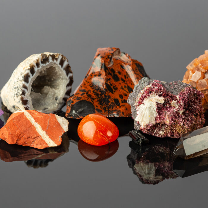 Close up photo of the Group of Stones and Minerals including Red Jasper, Aragonite Sputnik, Erythrite Crystals, Mahogany Obsidian and Agate Geode on Reflective Surface