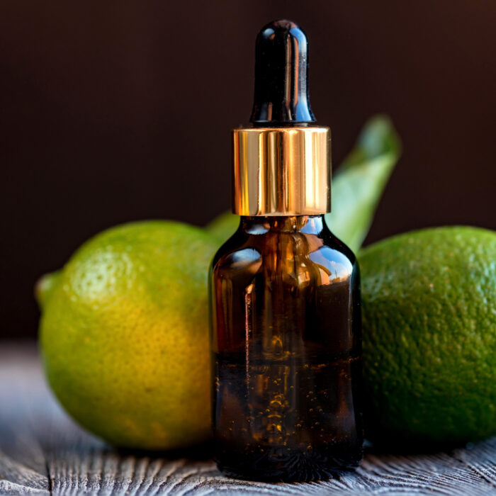 A dropper bottle of lime essential oil. Limes on the wooden rustic background