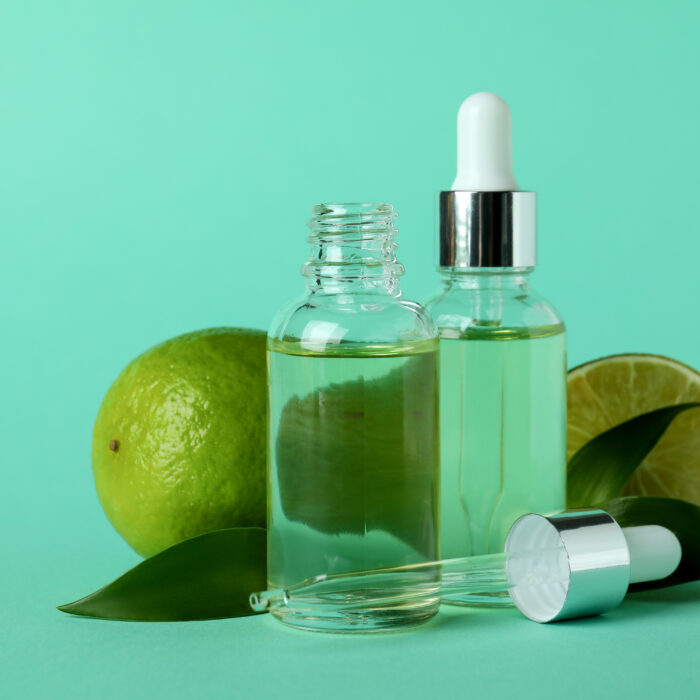Dropper bottles with oil and limes on mint background