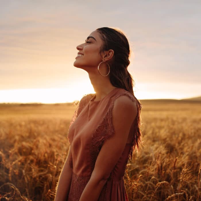 Young woman in the wheat field looking relaxed. Female in an agricultural field during sunset.