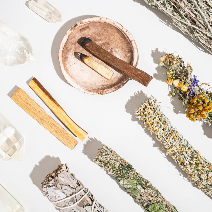 Items for spiritual cleansing - sage and aromatic herbs bundles, palo santo incense sticks and quartz crystals on white background. Top view. Flat lay