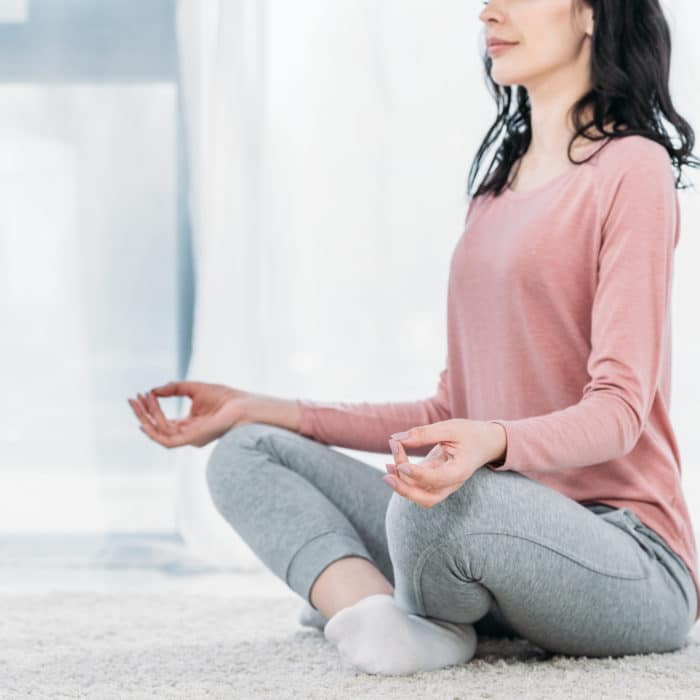 Cropped view of woman in Lotus Pose practicing meditation at hom