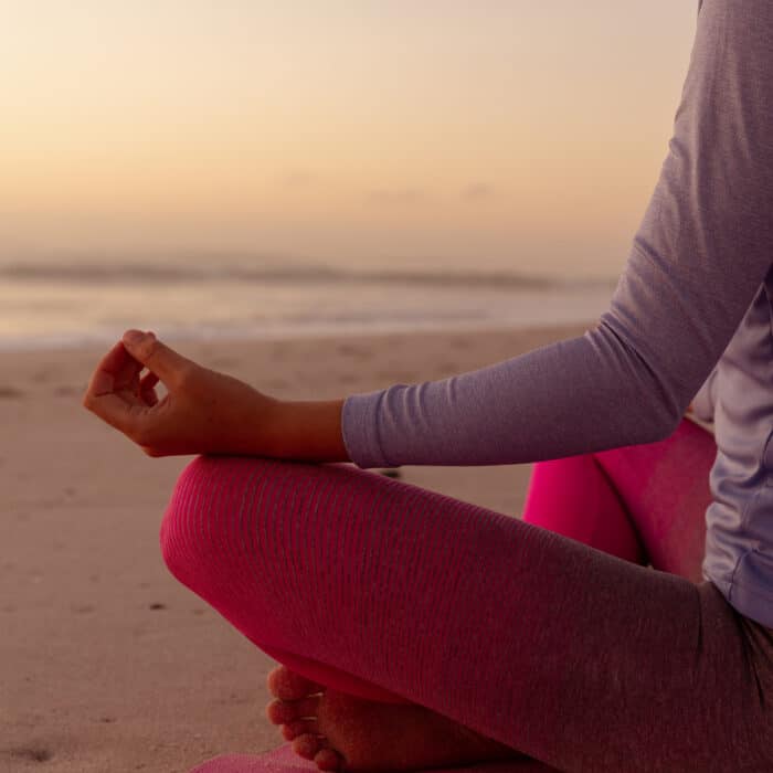 Mid section view of a Caucasian woman wearing sports clothes, enjoying time at the beach on a sunny day, practicing yoga, meditating in lotus position