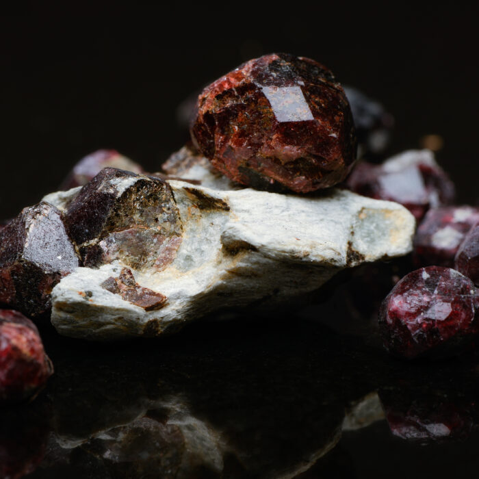 Closeup of uncut garnets with several in matrix on a dark reflective background.