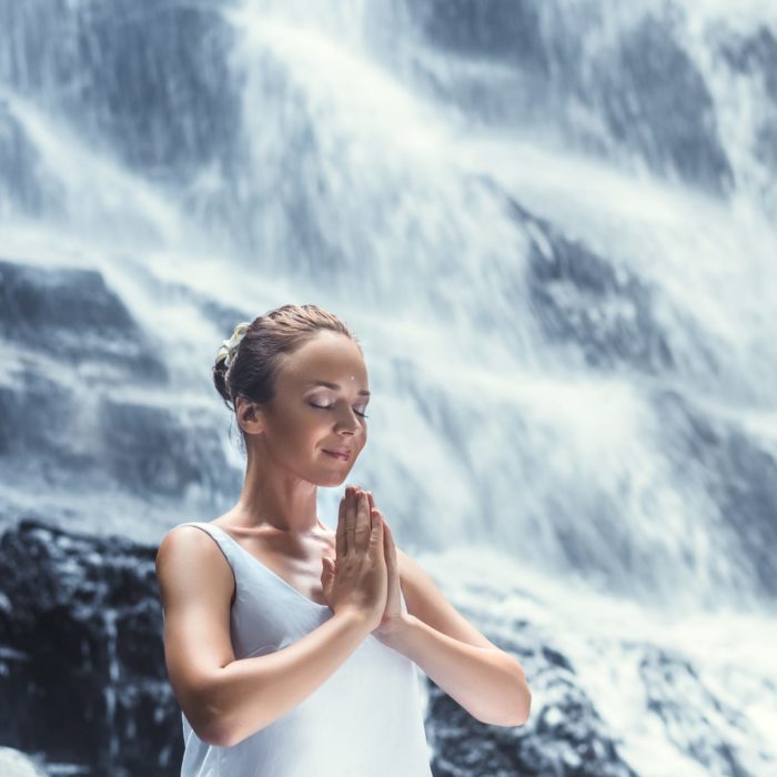 woman doing meditation near a waterfall