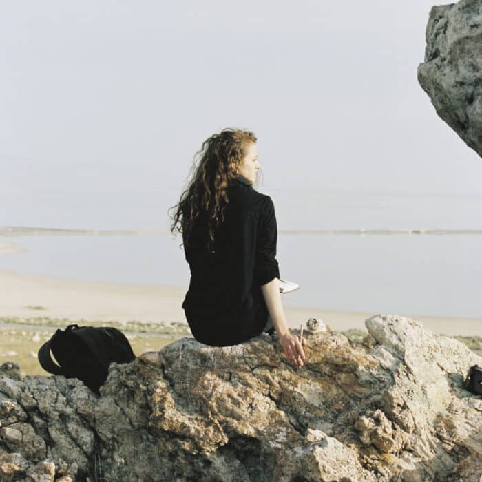 A woman sitting on a rock looking out over water.