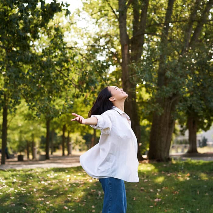 Carefree asian girl dancing, feeling happiness and joy, enjoying the sun on summer day, walking in park with green trees