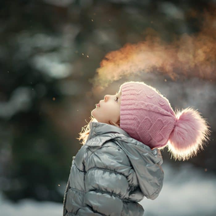 girl wearing puffer and beanie blowing cold air in the winter