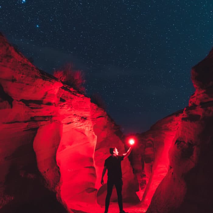 man holding red flare in the middle of a canyon