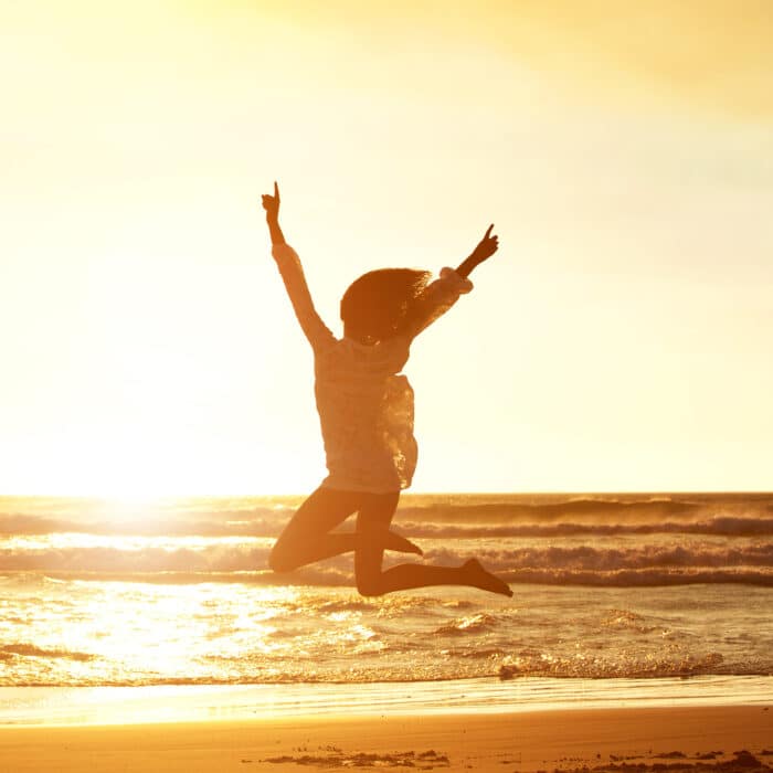 Silhouette portrait of young woman jumping for joy at beach during sunset