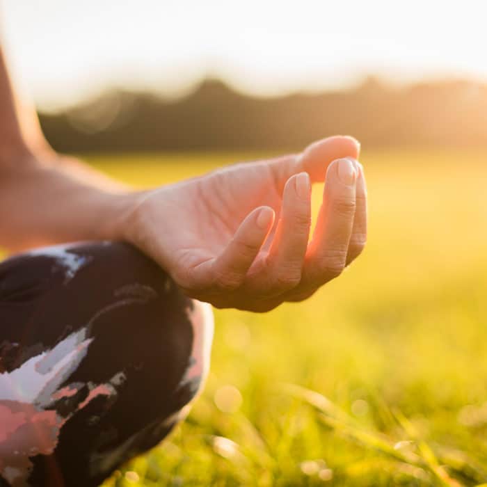 Detail of woman in lotus position on rural meadow at sunset, woman meditating
