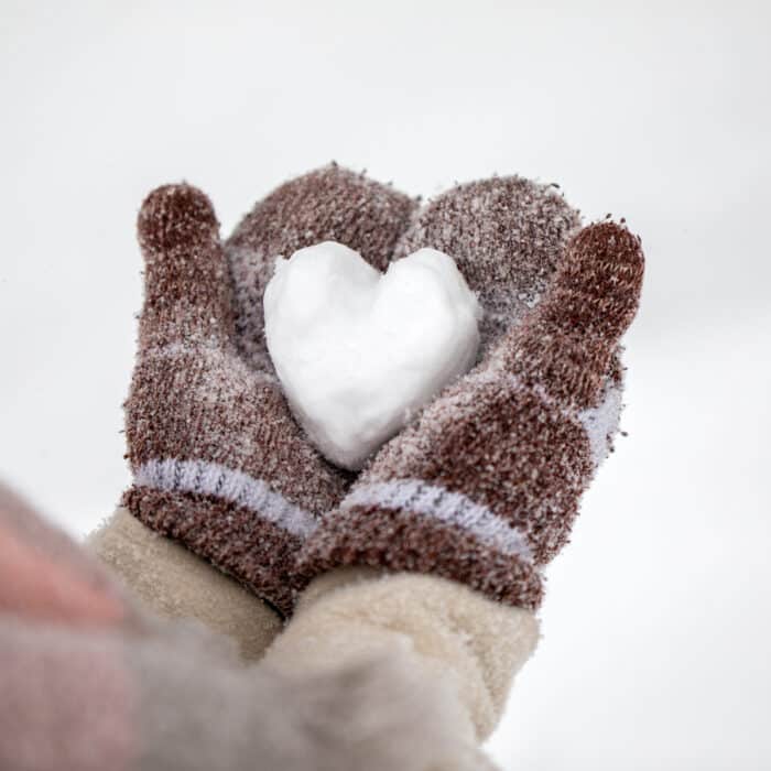 Female hands in knitted gloves holds snowy heart in winter day