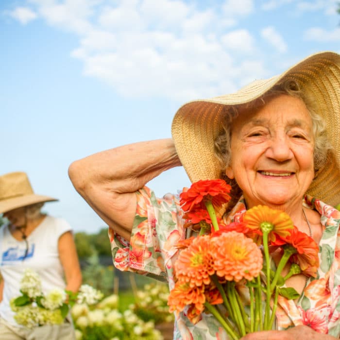 old woman smiling while holding flowers on a field