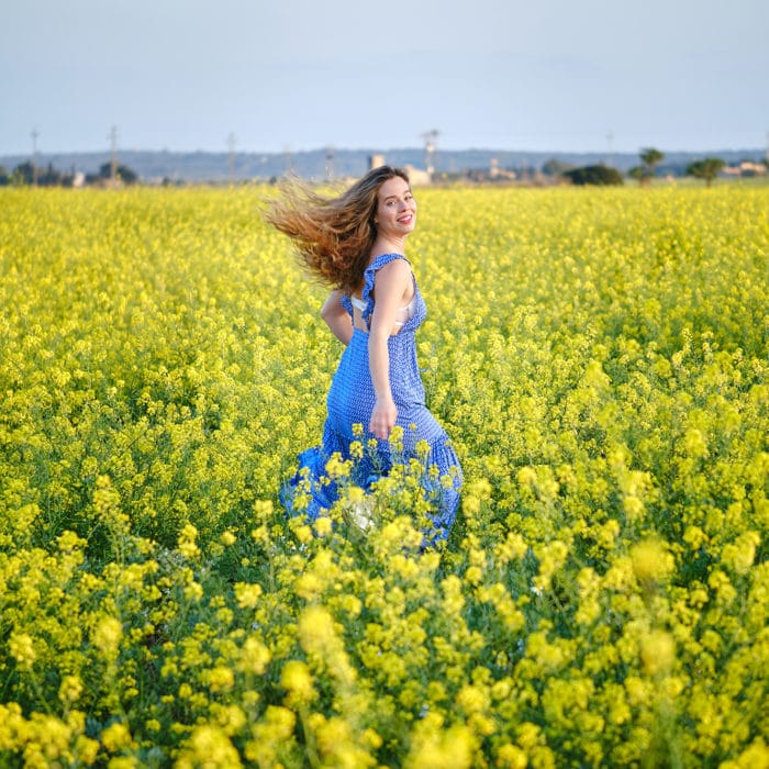 Joyful woman in sundress walking on blossoming meadow