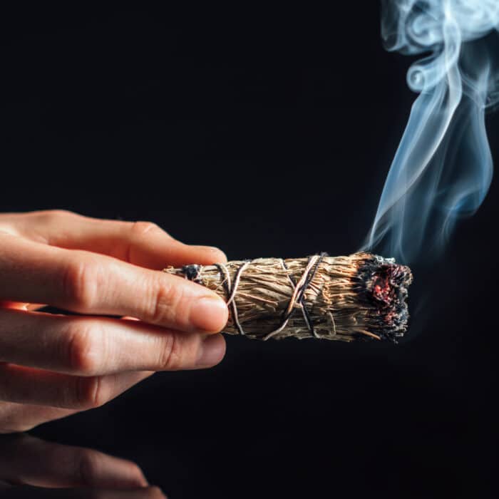 Smudging. Burning bundle of dried herb sage, black reflective background. Cleansing negative energy and purifying space.