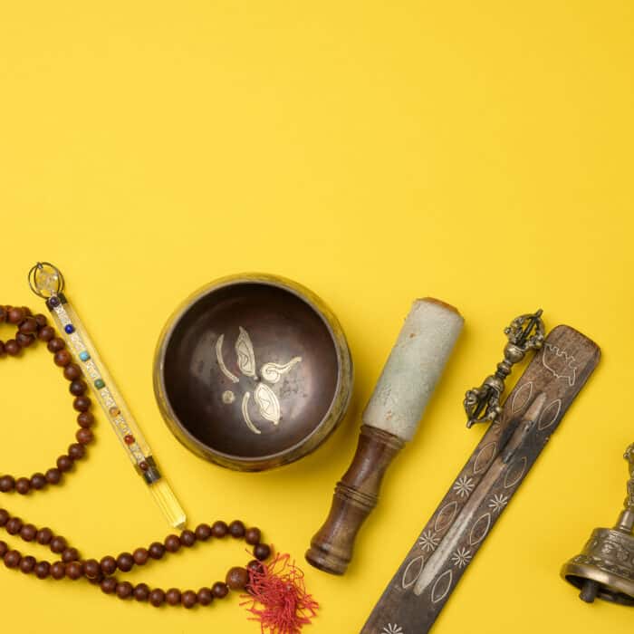 Tibetan singing copper bowl with a wooden clapper on a yellow background, objects for meditation and alternative medicine, top view, copy space