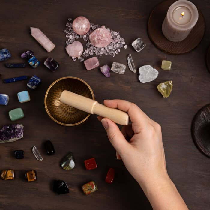 Woman cleansing healing chakra crystals with tibetan singing bowl. Rituals with gemstones and aromatherapy for wellness, healing, meditation, destress, relaxation, mental health, spiritual practices. Energetical power concept