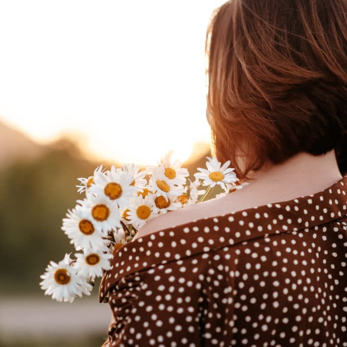 woman wearing brown polka dots holding flowers at sunset