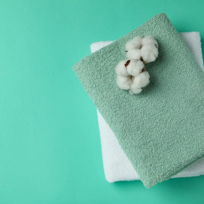 Clean folded towels and cotton on mint background