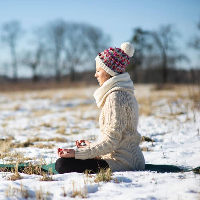Young athletic woman sitting and meditatingin the yoga pose on the snowy field during winter or early spring walk