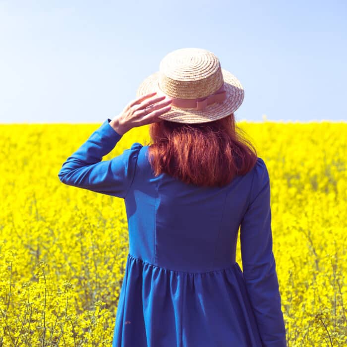 Happy girl in a hat walking in amazing field of yellow rapeseed in the countryside.
