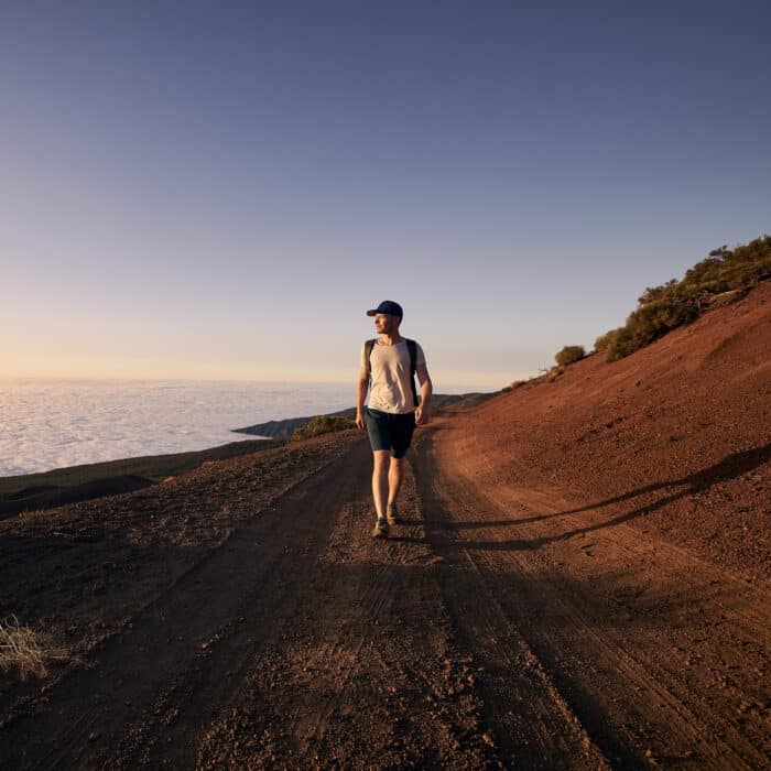 Man enjoyment view above clouds. Young hiker walking on dirt road against landscape at sunset.Tenerife, Canary Islands, Spain.