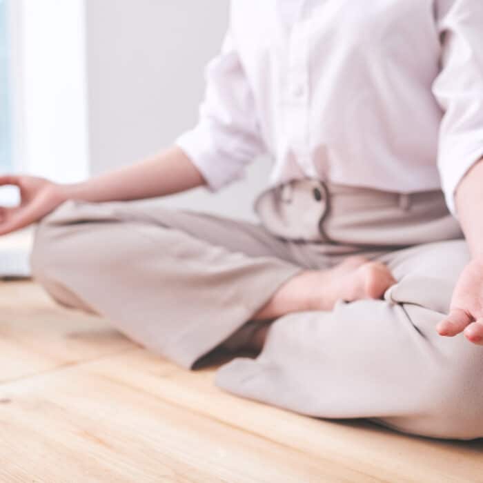 Close-up of unrecognizable businesswoman sitting in lotus position and holding hands in mudra while practicing relaxing meditation at workplace