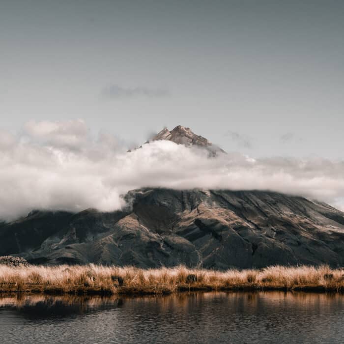 soft vegetation surrounding the lake and the impressive mountain in a beautiful nature landscape accompanied by a sky with many clouds, taranaki, new zealand