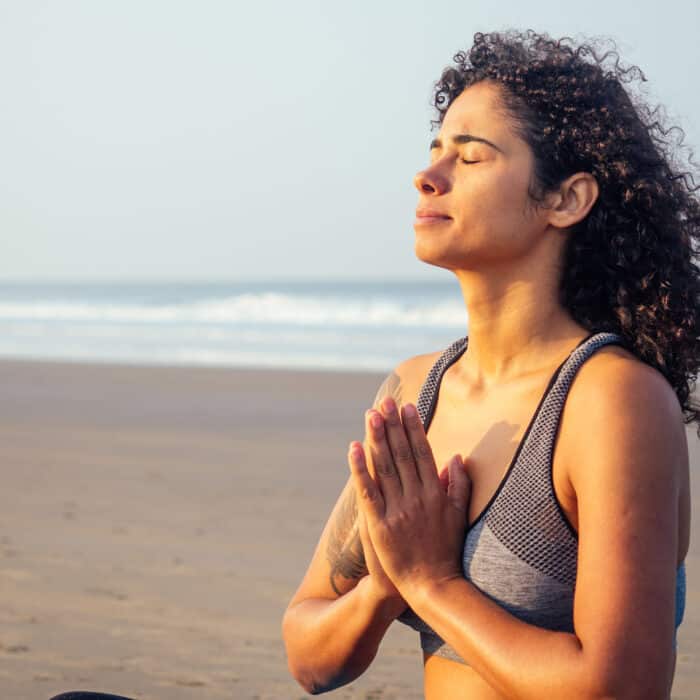 Afro america woman with curly hair and closed eyes deep breathing and calming herself on empty morning beach after surya namaskar