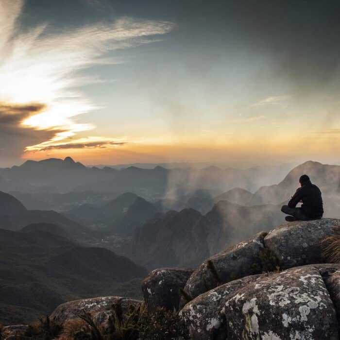 Rear View Of Man Sitting On Mountain During Sunset