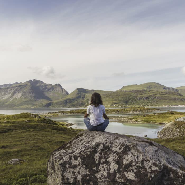 Young woman sitting on a rock, looking at view, meditating, Lapland, Norway