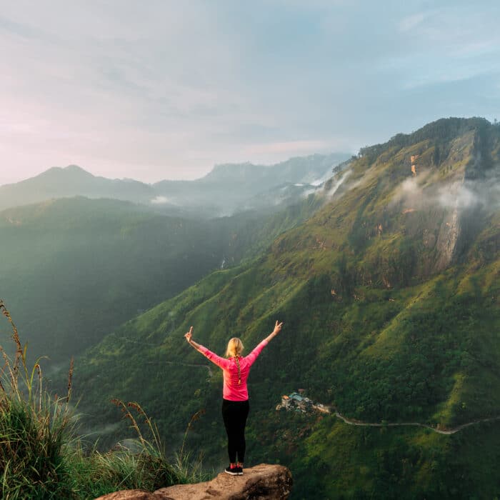 Girl meets sunrise in the mountains. Girl traveling to Sri Lanka. Mountain sports. Athlete happy finish. Mountain tourism. Walking tour. The journey to the mountains. Nordic walking