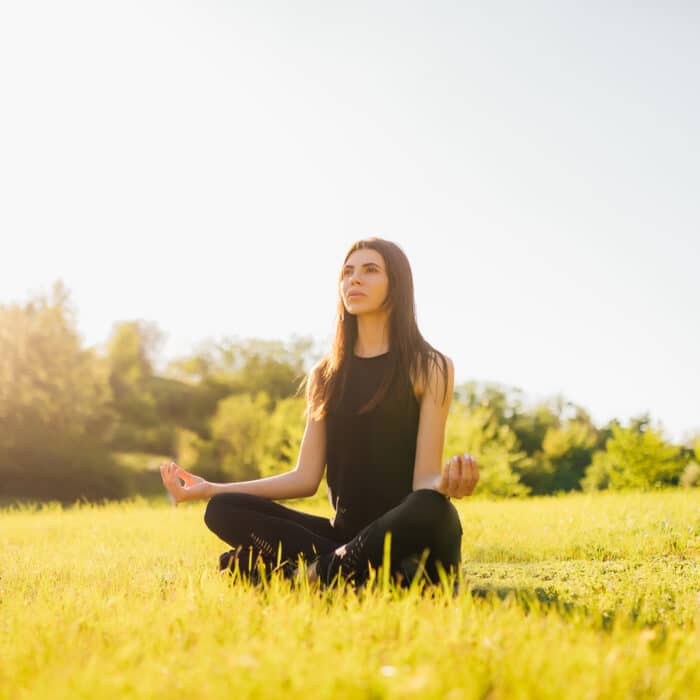 Woman meditates sitting on the grass, doing yoga at sunset