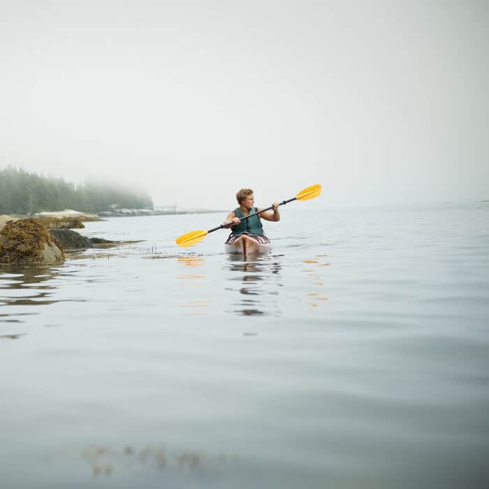A man paddling a kayak on calm water in misty conditions. New York State, USA