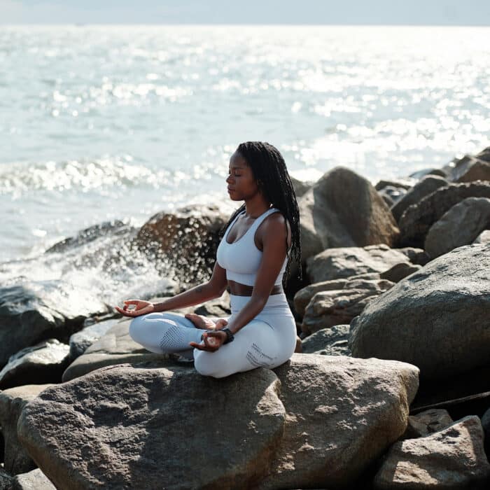 Beautiful fit young woman sitting on rocks in lotus position enjoying meditation and sound of waves