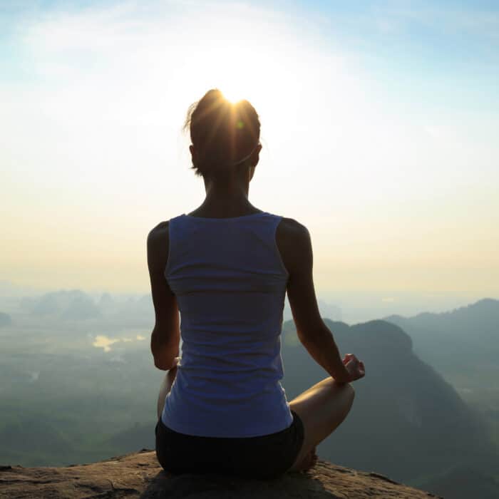 Young fitness woman meditating on sunrise mountain peak