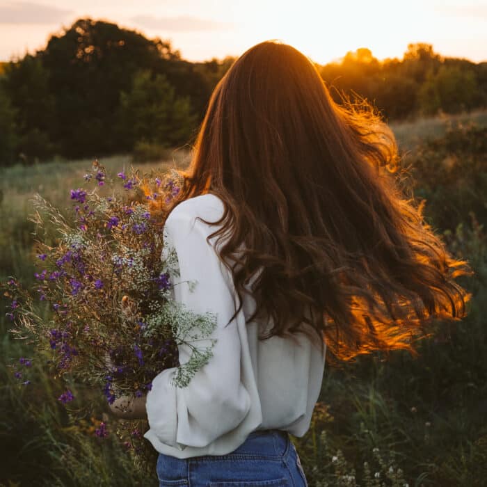 National Relaxation Day, relaxation practices, mental health, slow living concept. Young girl with long windy hair and flower bouquet enjoying nature on the background of sunset.