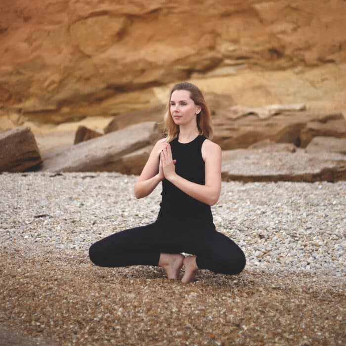 Woman practices yoga by the sea on a cliff background.
