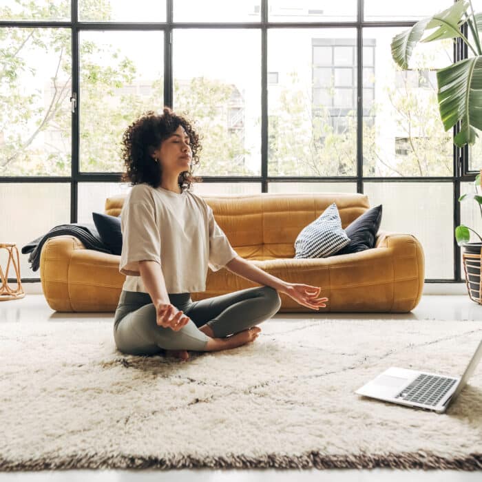 Young multiracial latina woman meditating at home with online video meditation lesson using laptop. Meditation and spirituality concept.