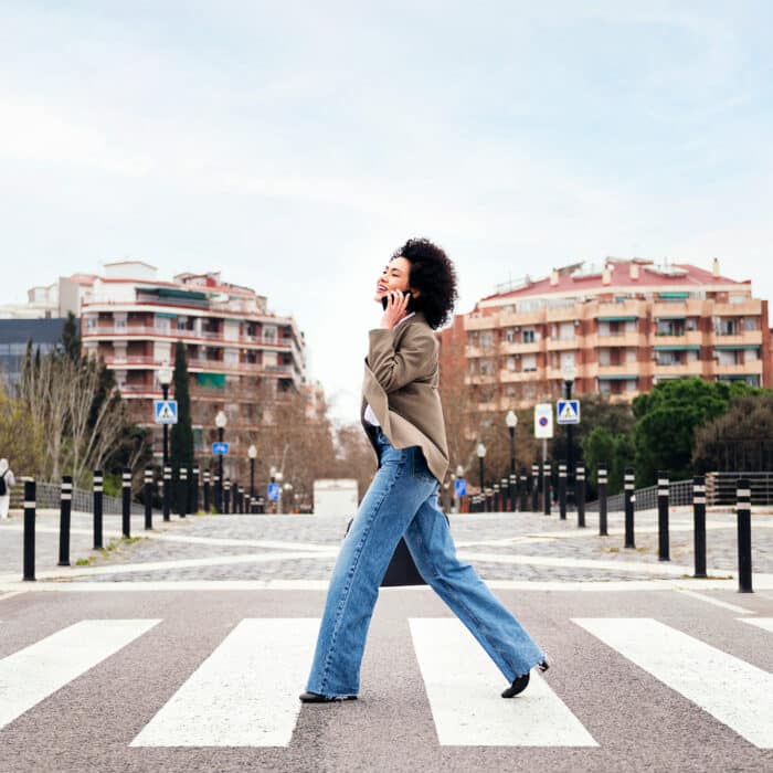 Smiling business woman walking on a crosswalk talking by mobile phone, concept of communication and urban lifestyle, copy space for text