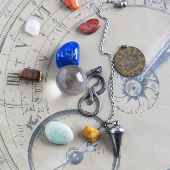 Semiprecious stones, pendulum, pendant and crystal ball on horoscope circle
