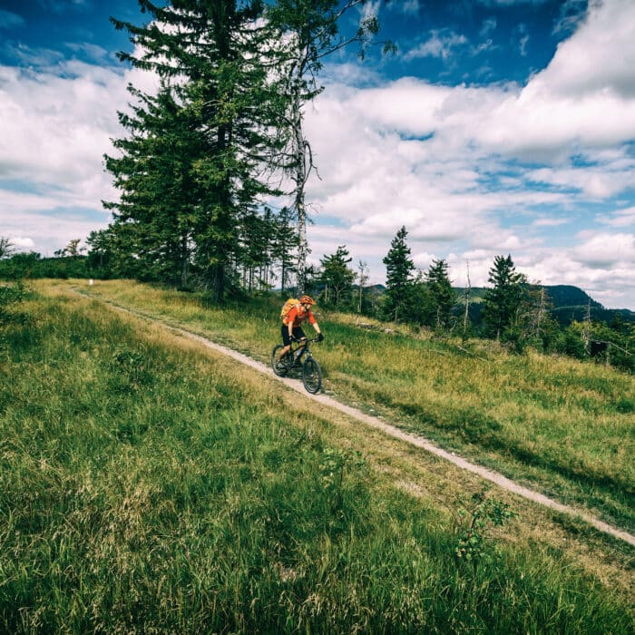 Mountain biking man riding on bike in summer inspirational mountains landscape. Rider cycling MTB on enduro trail path. Sport fitness motivation and inspiration. Rider mountain biker in summer woods.
