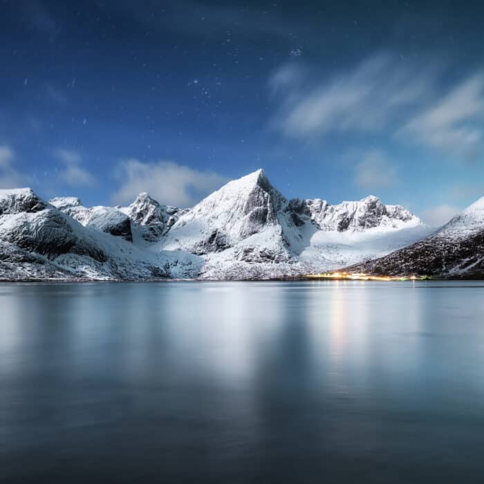 Mountains and reflections on water at night. Winter landscape. The sky with stars and clouds in motion. Nature as a background. Norway - travel