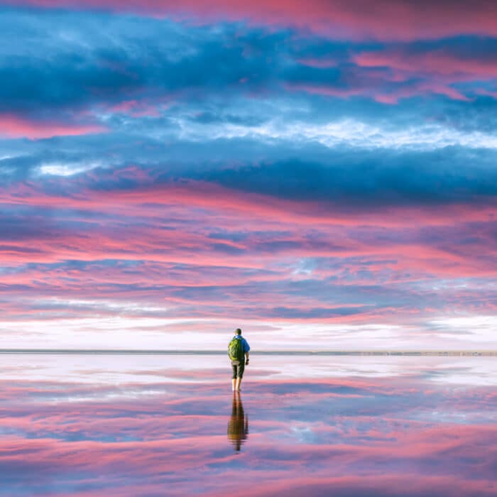 A tourist stands in calm water, which reflects the incredible purple sunset sky. Landscape photography