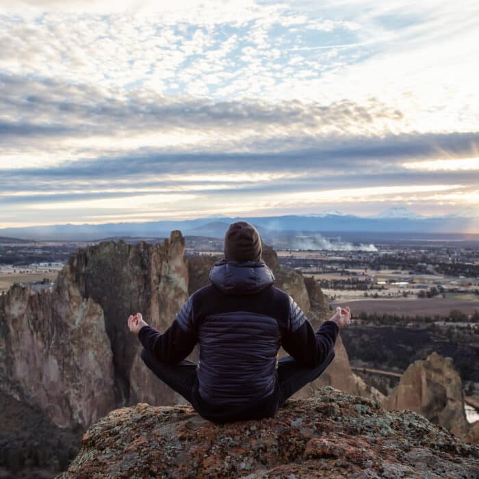 Adventurous man sitting in a meditation pose on top of a cliff during a vibrant sunset. Taken in Smith Rock, Oregon, America. Concept: adventure, freedom, travel, holiday, vacation