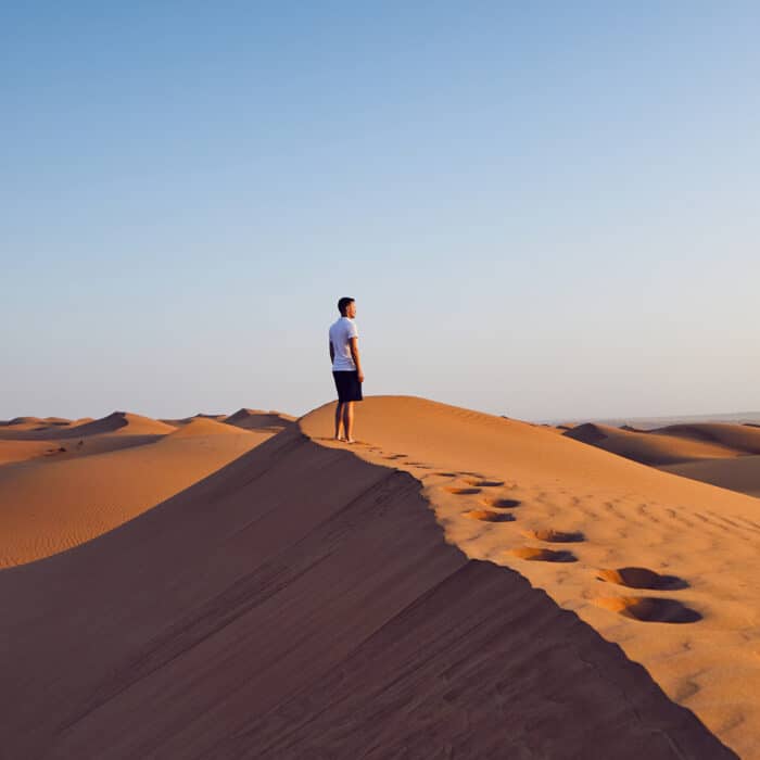 Young man standing on top of sand dune and looking at view. Desert Wahiba Sands in Oman.