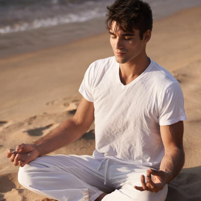 Connecting with the universe. Shot of a young man doing yoga at the beach